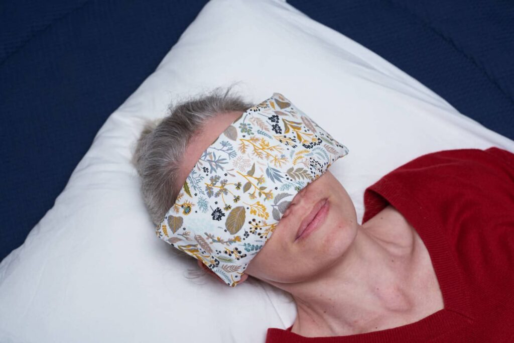 Head shot of woman laying on a white pillow, an eye pillow covers her eyes