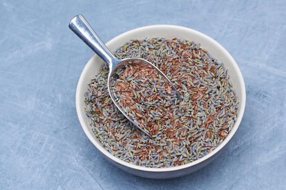 bowl with spoon, filled with a mixture of flaxseed and dried lavender on a grey back ground