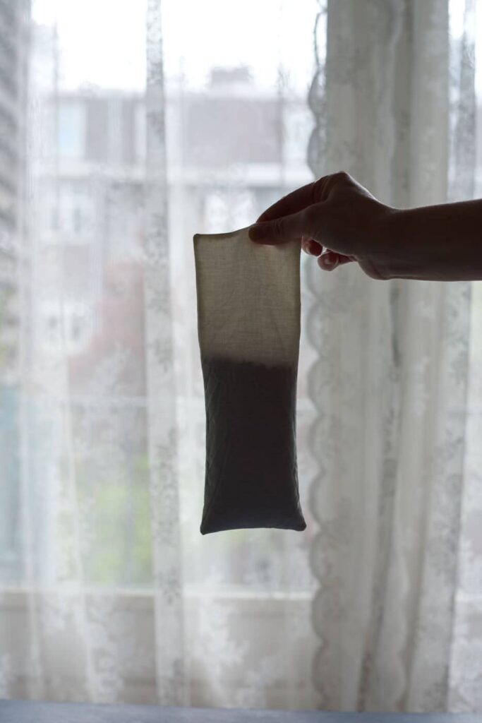 hand holding an eye pillow filled halfway with backlight from the window