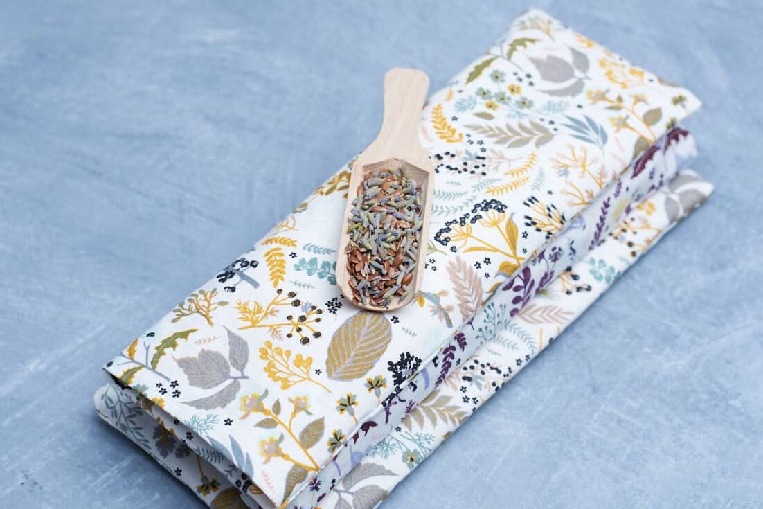 stack of three eye pillows. A little wooden spoon with mixture of flaxseed and dried lavender on top