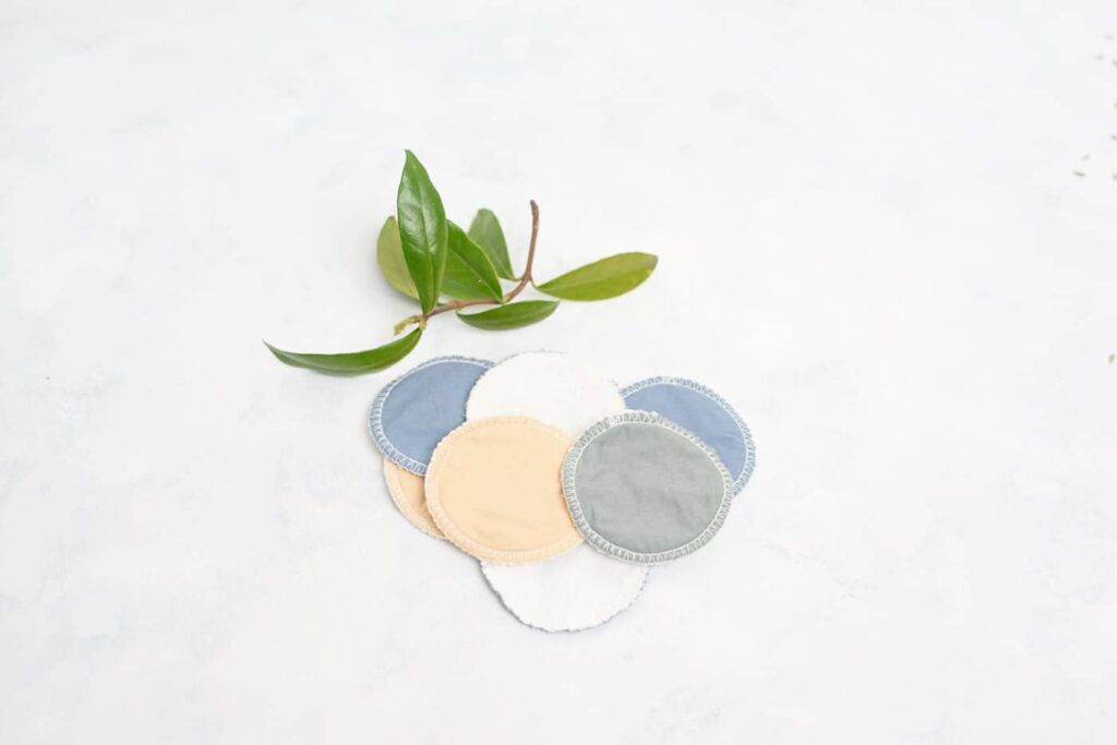 flatlay of eight facial rounds on a white background with green leaves at the side