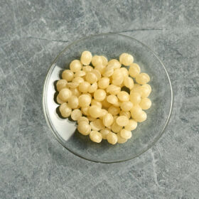 unrefined beeswax pellets on a small glas dish