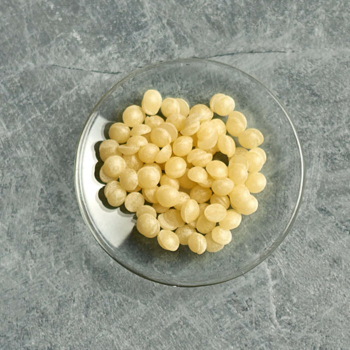 unrefined beeswax pellets on a small glas dish